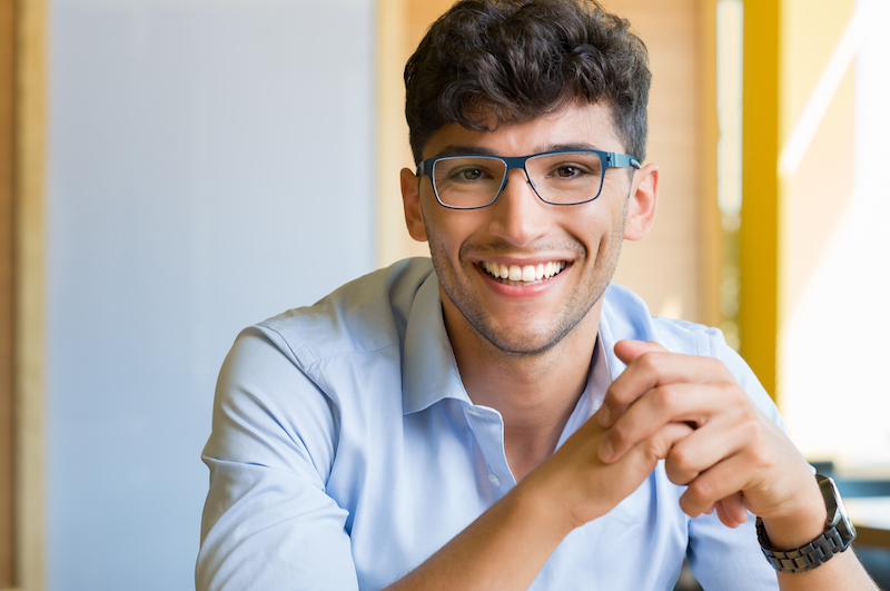 Closeup shot of young man wearing spectacle. Portrait of a guy with shirt and eyeglasses looking at camera indoor. Handsome smiling young man wearing blue spectacle.